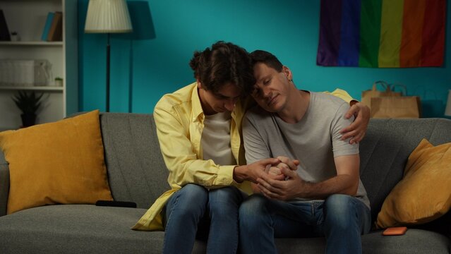 Shot of a homosexual couple sitting on the couch together, hugging, comforting each other, holding hands, expressing love and affection.