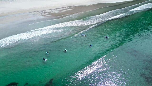 Waves on the beach with a group of surfers padling in the turquoise water. Hoddevik.