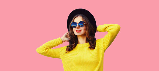Portrait of modern stylish young woman wearing black round hat, sweater on pink studio background