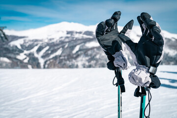 Close up of ski gloves on ski poles on top of a mountain range covered with bright white snow....