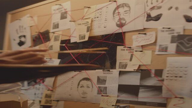 Vertical shot of unrecognizable agents using newspaper clippings, crime scene photos, suspects identikits and handprints while analyzing investigation board on wall in office