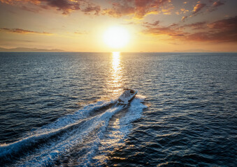 Aerial view of a motorboat cruising with speed over the sea into the sunset - obrazy, fototapety, plakaty