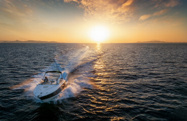 Aerial front view of a speedboat cruising over the sea during sunset time with copy space