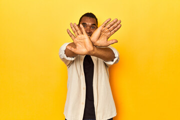 African American man with shirt, yellow studio, doing a denial gesture