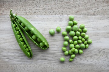 Garden peas (Pisum sativum) and two open pea pods isolated on a wood background. Landscape orientation.