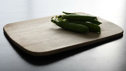 Garden pea (Pisum sativum) pods on a wooden chopping board, in a pile. Landscape orientation, view from the side. - obrazy, fototapety, plakaty