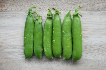 A line of garden pea pods (Pisum sativum), isolated on a wood background. Landscape orientation.