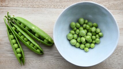 Garden peas (Pisum sativum) in a blue ceramic bowl with pea pods, on a wooden chopping board. Isolated on a white background. Landscape orientation. - obrazy, fototapety, plakaty