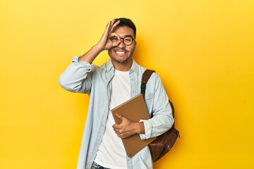 Asian student with backpack and notebook, yellow studio backdrop excited keeping ok gesture on eye. - obrazy, fototapety, plakaty