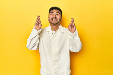 Asian man in crisp white shirt on yellow studio crossing fingers for having luck