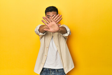 Casual Asian man with open shirt, white tee on yellow studio doing a denial gesture