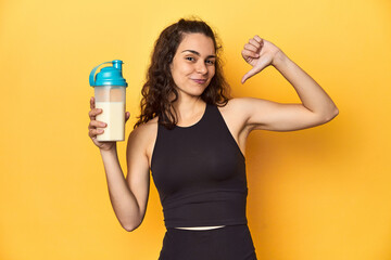 Woman holding a protein shake, in sportswear, feels proud and self confident, example to follow.