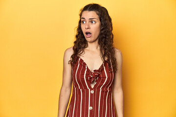 Young Caucasian woman, yellow studio background, being shocked because of something she has seen.