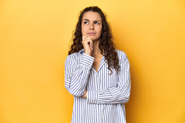 Young Caucasian woman, yellow studio background, thinking and looking up, being reflective, contemplating, having a fantasy.