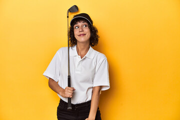 Athletic Caucasian woman with curly hair golfing in studio dreaming of achieving goals and purposes