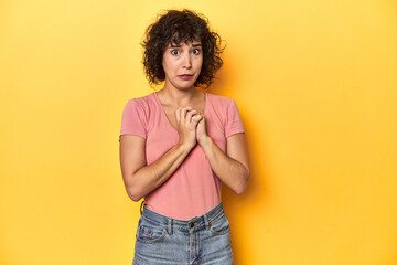 Curly-haired Caucasian woman in pink t-shirt scared and afraid.