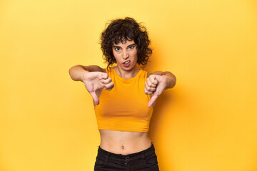 Curly-haired Caucasian woman in yellow top showing thumb down and expressing dislike.