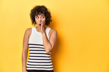 Caucasian curly-haired woman in white tank-top is saying a secret hot braking news and looking aside