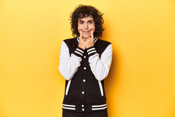 Curly-haired Caucasian woman in baseball jacket doubting between two options.