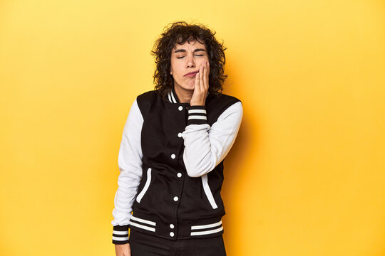 Curly-haired Caucasian woman in baseball jacket having a strong teeth pain, molar ache.