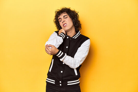 Curly-haired Caucasian woman in baseball jacket massaging elbow, suffering after a bad movement.