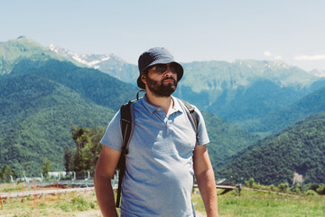 Naklejka premium millenial bearded tourist man wearing bucket hat, with backpack trekking in mountains