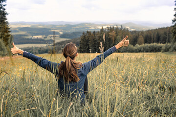 Happy young woman enjoying time in nature country setting with thumbs up looking out at peaceful view  - obrazy, fototapety, plakaty