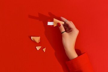 Women hands with manicure holding fortune cookie on red background. Blank paper for prediction words - obrazy, fototapety, plakaty