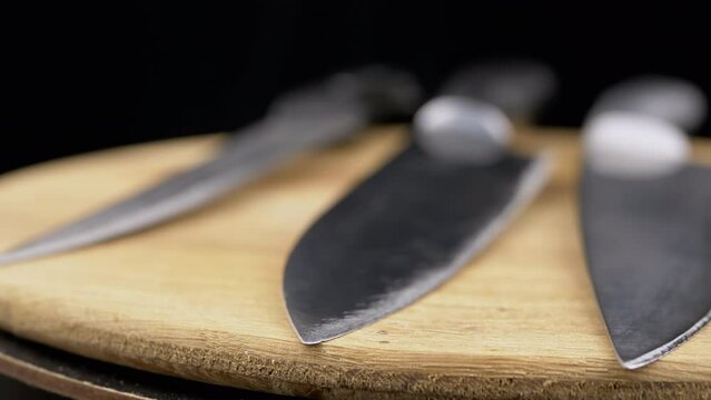 Close up, Set of Knives Rotate on a Wooden Turntable on a Black Background. Sharp blades of steel kitchen knives. Professional knives for the chef. Cutlery. Wooden background, blur. Cooking concept.