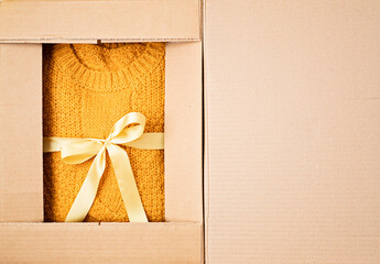 Unpaking delivery box with warm orange sweater inside. Online shopping, gifts for fall and winter seasonal holidays, christmas