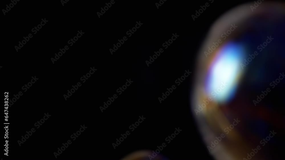 Poster colorful soap bubbles fly in an empty space on isolated black background. three large rainbow bubble