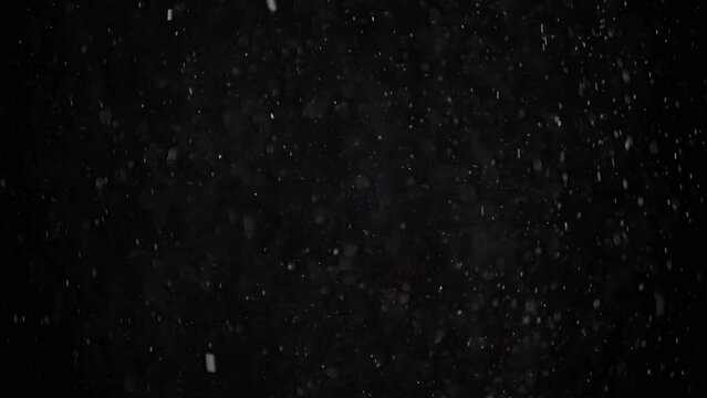 Slowly Falling Stream of Particles of Dust, Snow, Tinsel on a Black Background. White spots of powder and flakes are mixed in the empty space. Stardust. Accumulation of gas, fog. Space. Slow motion.