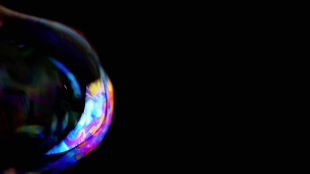 Close up, Large Colorful Soap Bubbles Slowly Fly on a Black Background. Transparent Rainbow bubbles in empty space. Blurred motion. Focus. Texture. Abstract. Slow motion, isolated. Game. Party