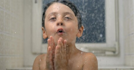 Happy child enjoying bath time with droplets falling in super 800 fps slow-motion, young boy beaming with joy observing water flow standing in shower