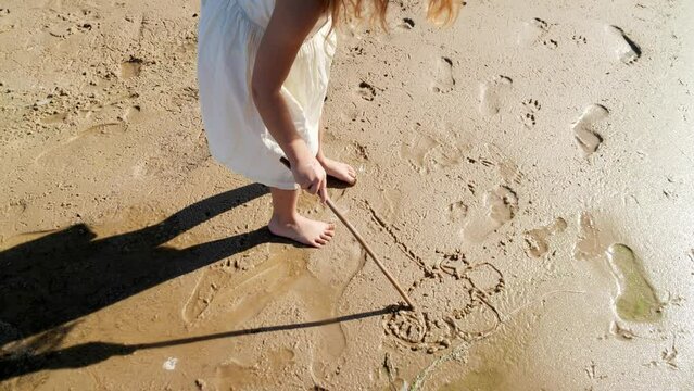 Girl child drawing with a stick on the sand on the beach and having fun