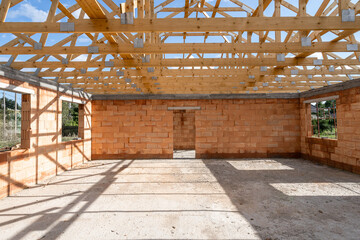 Unfinished house with red brick walls under wooden roof beams