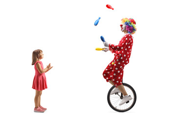 Little girl clapping and watching a clown riding a unicycle and juggling