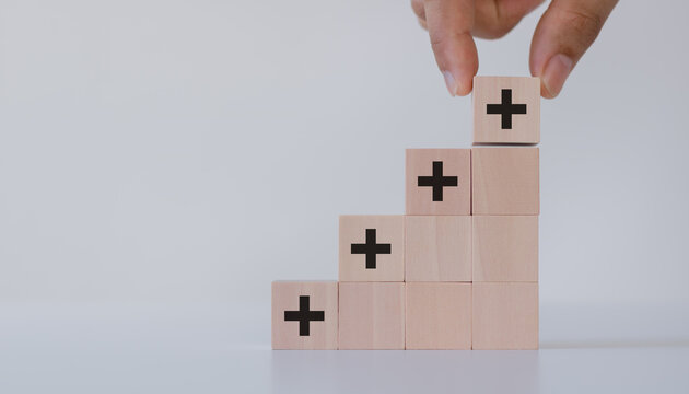 Hand putting the wooden cubes with plus sign to offer positive things. Positive things, added value, benefits, additional, personal development, growth mindset, positive thinking, opportunities.