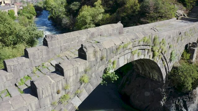 Forward reveal aerial shot of medieval Sanahin bridge over Debed river on sunny summer day. Alaverdi, Lori Province, Armenia.