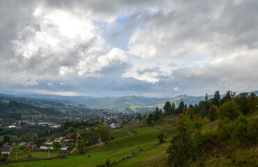 Fototapeta premium Picturesque autumn scenery of rolling countryside with houses of a mountain village on green hills. Vorokhta, Carpathian Mountains, Ukraine