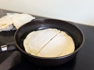 two pasties are fried in a cast iron frying pan next to frozen pasties in cling film, fast food