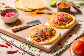 Fototapeta na wymiar Tacos mexicanos de carnitas y tinga de pollo, sobre tabla de madera en una composición sobre mesa de restaurante grill con limones, tortillas, chiles y verduras con tajin