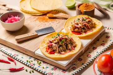 Tacos mexicanos de carnitas y tinga de pollo, sobre tabla de madera en una composición sobre mesa...