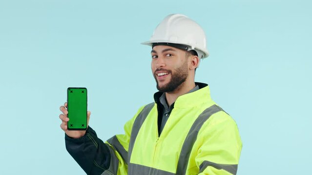 Construction man, green screen phone and studio with pointing, app promo or face by blue background. Engineer, maintenance employee or contractor for smartphone mockup, tracking markers or logo on ux
