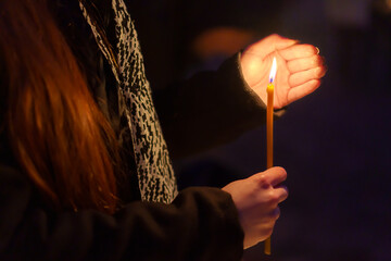 A candle in the hands of a praying woman. Symbolic concept. Background with selective focus