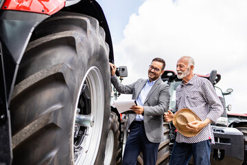 Professional salesman showing farmer new modern tractor. Selling agricultural machines. - obrazy, fototapety, plakaty