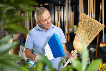 Positive middle-aged male customer choosing between two brooms in a hardware store