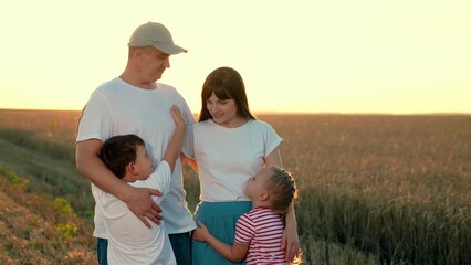 Happy young family of farmers is hugging their son daughter. Happy mom dad baby cuddling in wheat field enjoying nature. Father, mother, boy girl embrace father mother walking outdoor. Family together