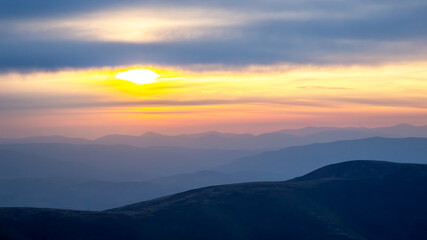 Colorful clouds in the sky at sunset against the backdrop of a mountainous forest area.