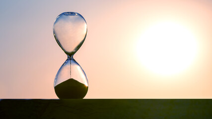 Hourglass counts the length of time against the background of the evening sun. The concept of the fluidity of life time in the universe. time and light - obrazy, fototapety, plakaty